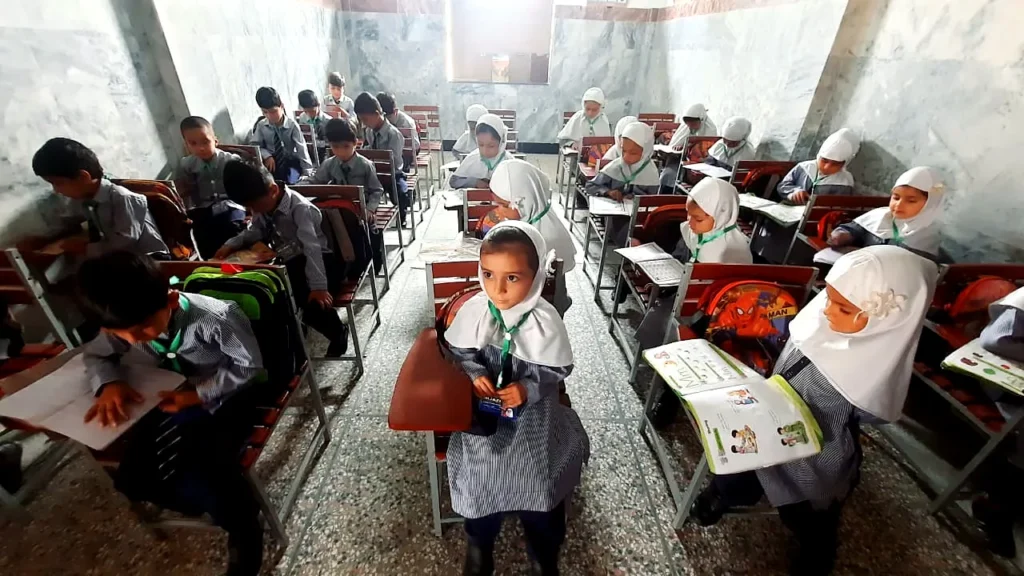 A classroom of girls in white scarves and boys in grey uniforms at their desks.