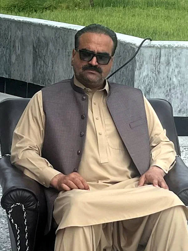 Founder Muhammad Sadiq Hijazi, seated outdoors in a beige shalwar kameez and grey waistcoat.